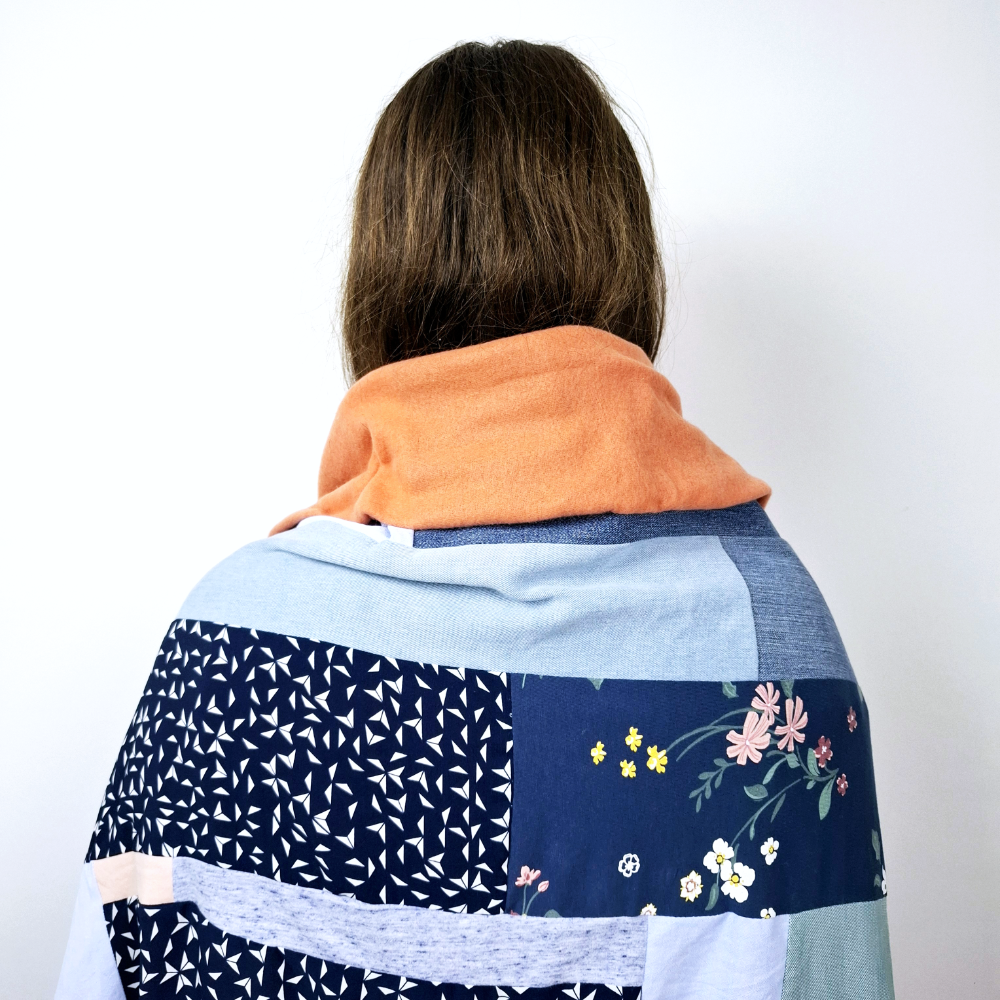 Mädchen steht mit dem Rücken zu uns und hat eine Patchworkdecke umgelegt, Individuelle Erinnerungsstücke und Trost aus Stoff aus Kleidung von Verstorbenen und geliebten Fellnasen. Nadine Miesenburg von der Blauzone