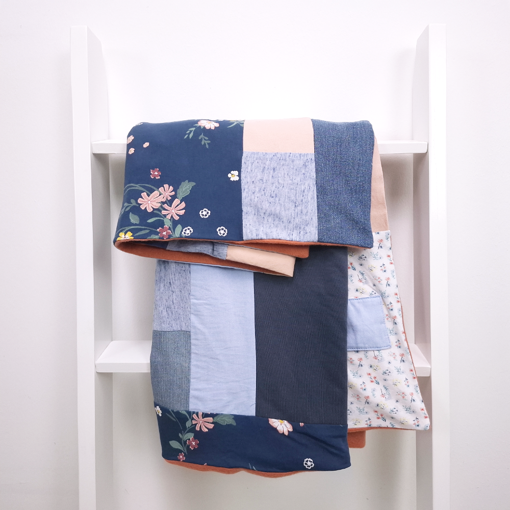 Blaue Patchworkdecke liegt über einer weißen Holzleiter, Individuelle Erinnerungsstücke und Trost aus Stoff aus Kleidung von Verstorbenen und geliebten Fellnasen. Nadine Miesenburg von der Blauzone